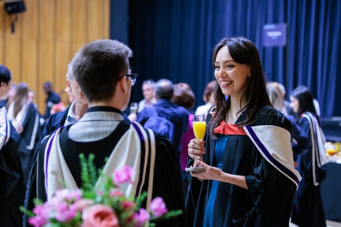 Two students in academic dress enjoying an orange juice at a Faculty Reception
