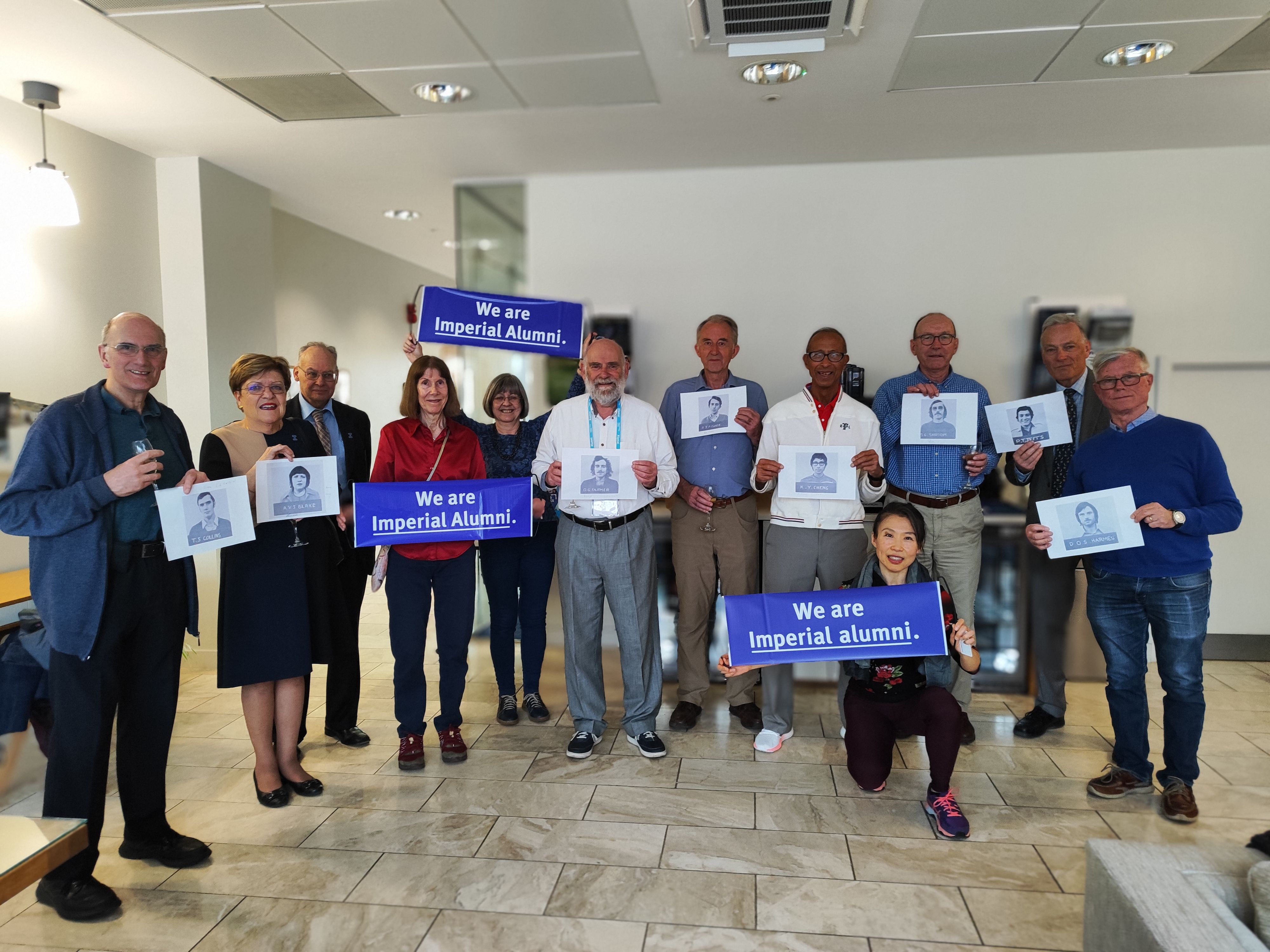 The group are gathered holding Imperial alumni branded signage and photos of their old student headshots